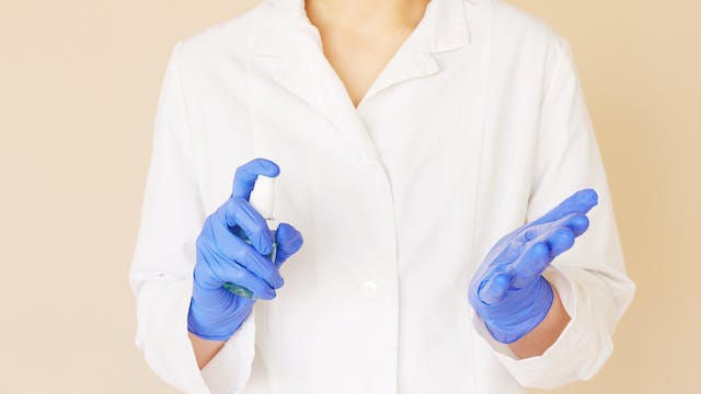 A healthcare professional using a spray hand sanitizer before a medical procedure