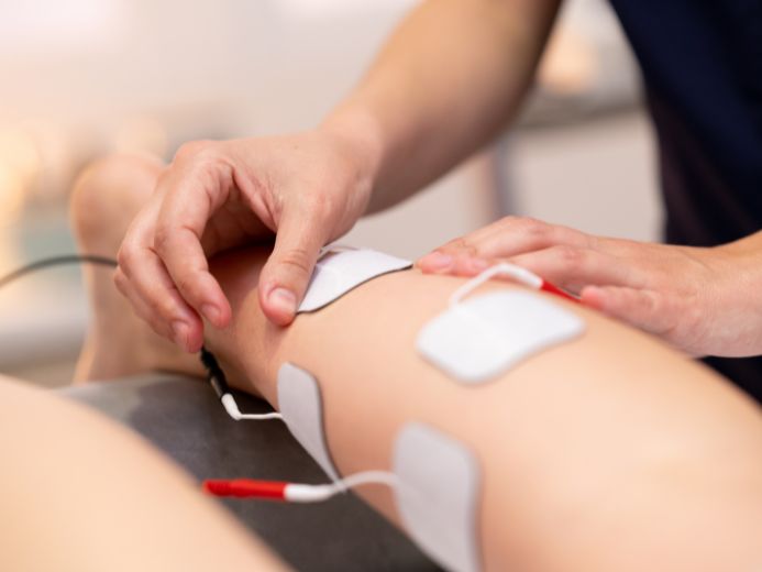 Physiotherapist positioning TENS units on a patient for pain relief and muscle rehabilitation