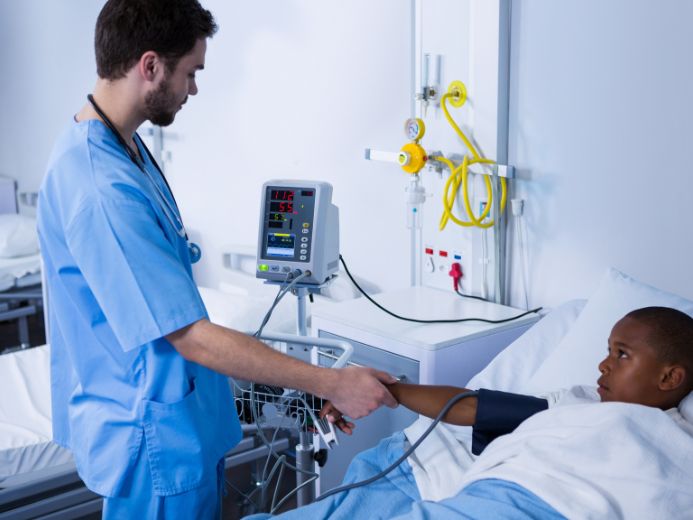 nurse using a blood pressure monitor on a young child in a hospital bed