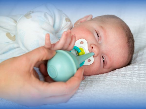 A mother is suctioning the baby’s stuffed nose with a bulb syringe